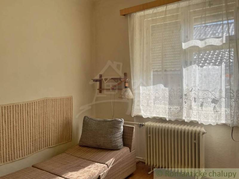 A simple room in a family house with a lounger and decorative curtains on the window.