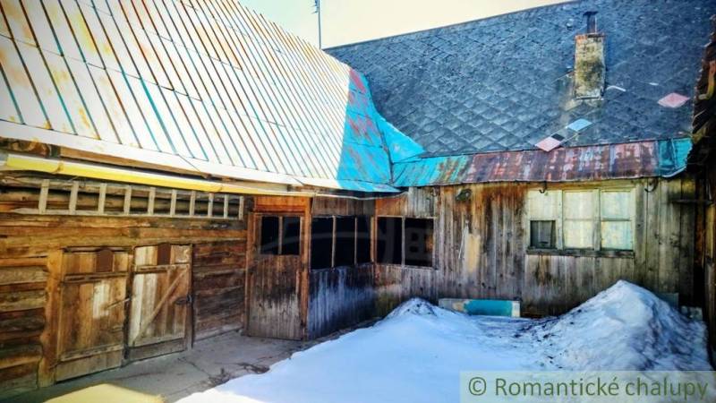 A wooden family house in Osturňa with a metal roof and remnants of snow in the yard.