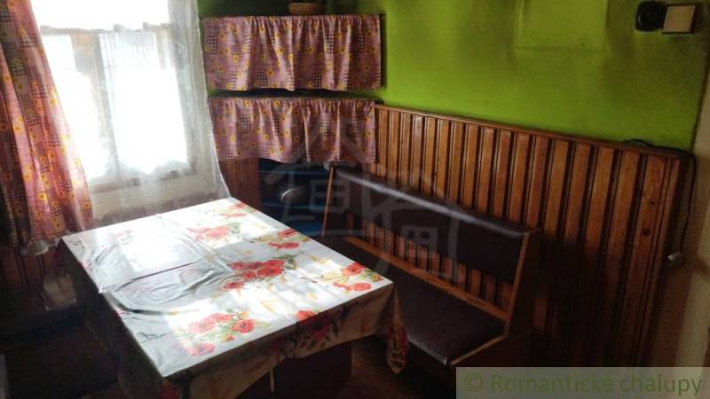 Dining area in a family house with wooden paneling, curtains, and a floral tablecloth.