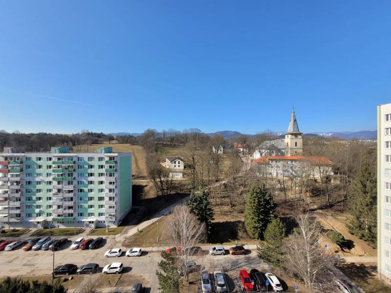 A view of Banská Bystrica from Kalinčiakova Street, next to a 2-room apartment, with a church and an apartment building.