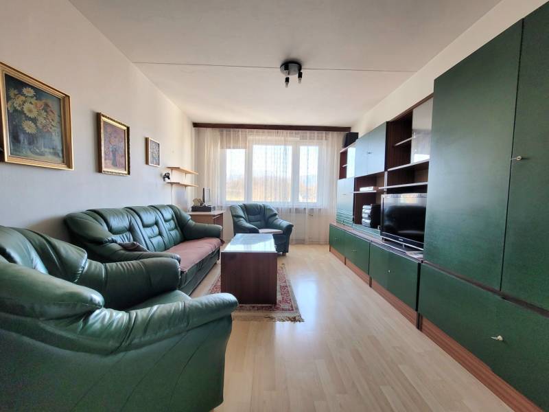 Living room in a two-room apartment with green sofas and a floor with a wood decor.