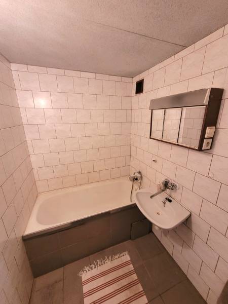 A bathroom with a bathtub and white tiles in a 2-room apartment.