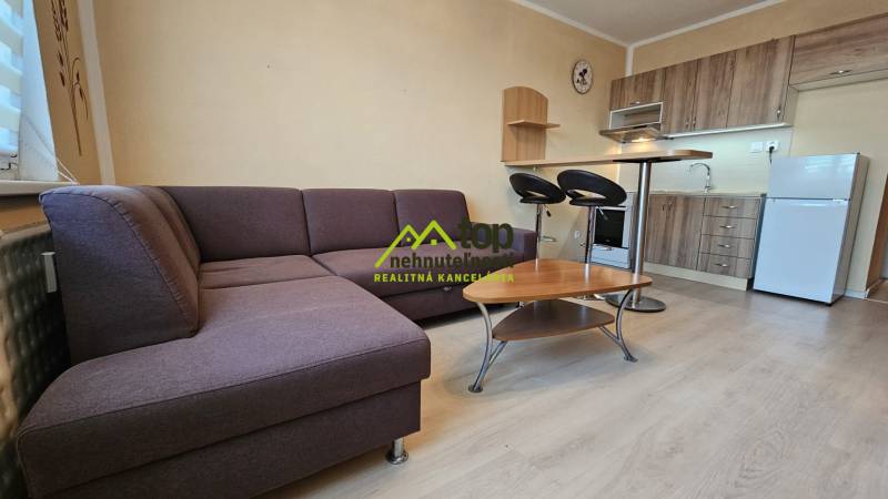 Studio apartment with a corner sofa, kitchen unit, and floor with a wood design.