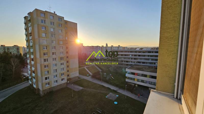 View from a studio apartment in Topoľčany, panel buildings, sunset, and a children's playground.