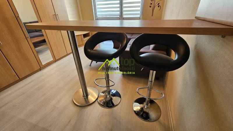 Studio apartment with a counter, chairs, and flooring with a wood finish.