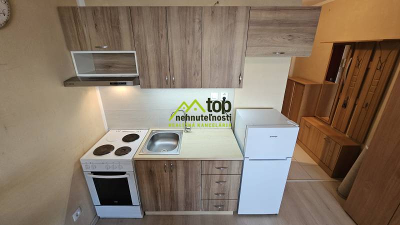 A kitchen in a studio apartment with a wooden decor floor and basic equipment.