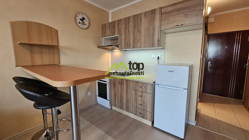 A kitchenette in a studio apartment with a wooden decor, table, chairs, kitchen cabinets.