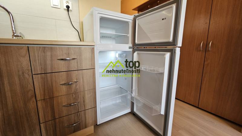 Studio apartment with a kitchenette and an open refrigerator, floor with wooden decor.
