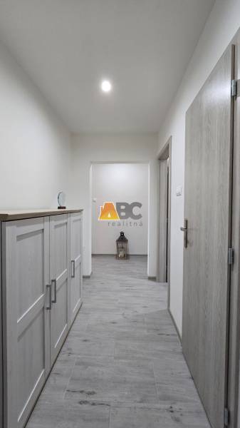 A hallway with a wood-patterned floor in a 2-room apartment, furniture on the left side.