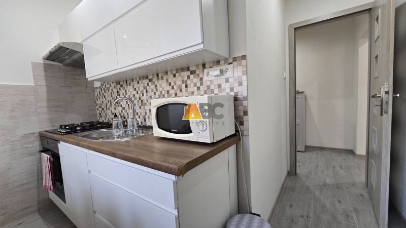 A kitchen in a 2-room apartment with white cabinets, a microwave, and wooden decor.