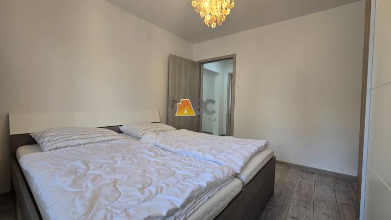 Bedroom in a 2-room apartment with a double bed, light-colored wall, and floor with wood decor.