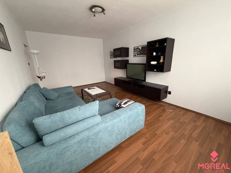 Living room with a TV, blue sofa, and wood-patterned flooring in a 3-room apartment.