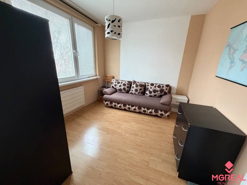 A room with a sofa, a dresser, and a wooden-patterned floor in a three-room apartment.