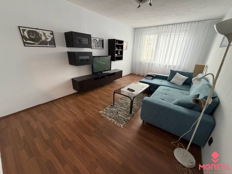 Living room with wood-patterned flooring and a sofa in a three-room apartment.