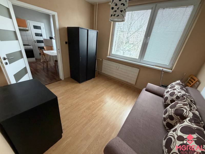 A room in a 3-room apartment with a wooden decor floor and simple furniture.