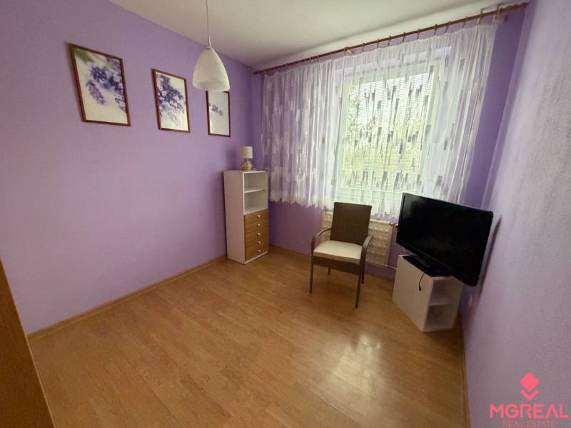 Purple room in a 3-room apartment with a wooden decor floor, an armchair, and a television.