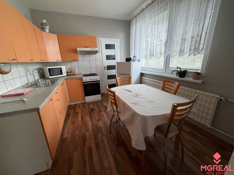 A kitchen with orange cabinets, a dining table, and a wood-patterned floor in a three-room apartment.