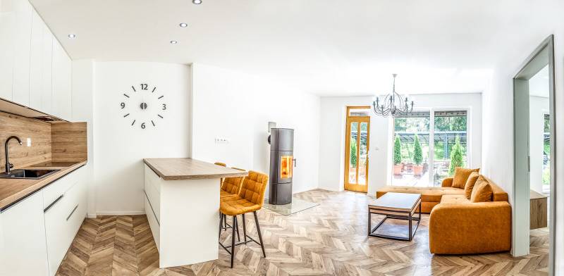 Bright holiday apartment with a kitchen, orange sofa, and wood-patterned flooring.