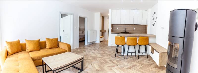 Recreational apartment with a sofa, kitchen counter, and wood-patterned flooring.
