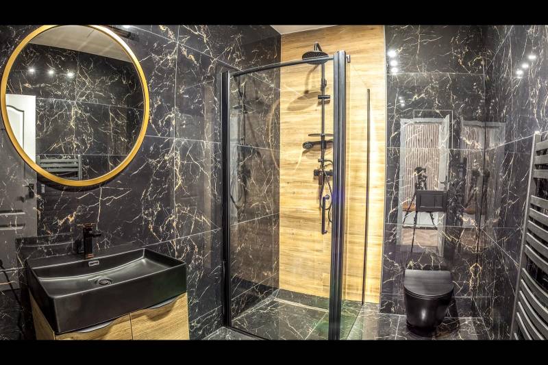 Bathroom in a holiday apartment with black tiles and a shower enclosure.