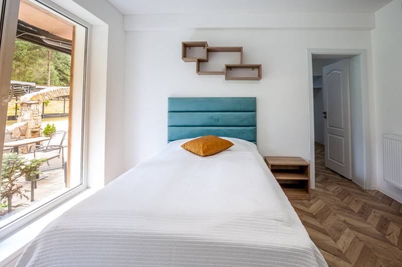 Single bed in a holiday apartment with a wooden decor floor and a large window.