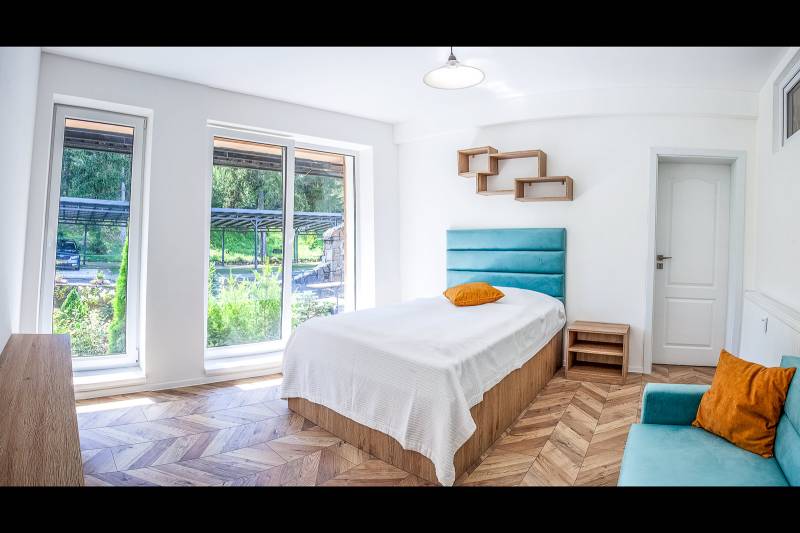 A bright room with a bed, large windows, and a wooden decor floor in a vacation apartment.