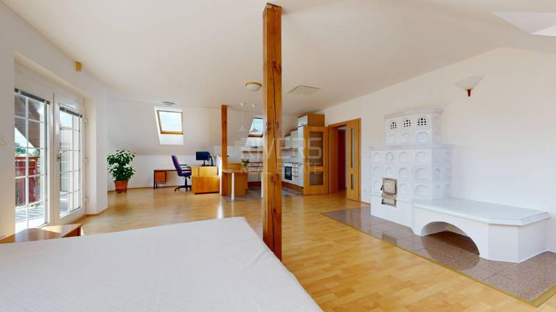 Attic interior of a family house with a tiled stove, a work corner, and a floor with a wooden decor.