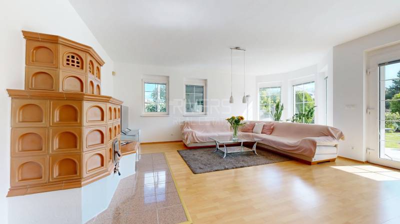 Living room in a family house with a tiled stove, sofa, and wooden decor flooring.