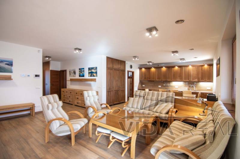 Interior of a family house with a spacious living room, kitchen unit, and wooden decor flooring.