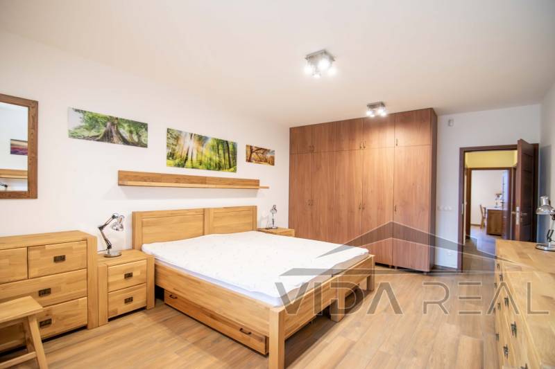 A bedroom in a family house with a bed, wardrobes, and a floor with a wooden decor.