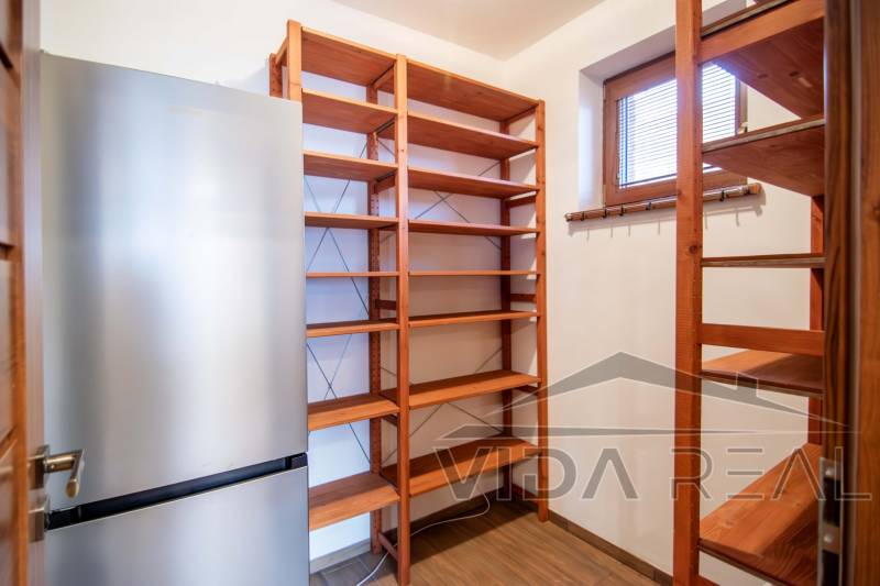Fridge and wooden shelves in the pantry of a family house with a wooden decor floor.