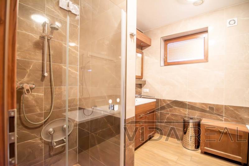 A bathroom in a family house with ceramic tiles and a shower enclosure, floor with a wooden decor.
