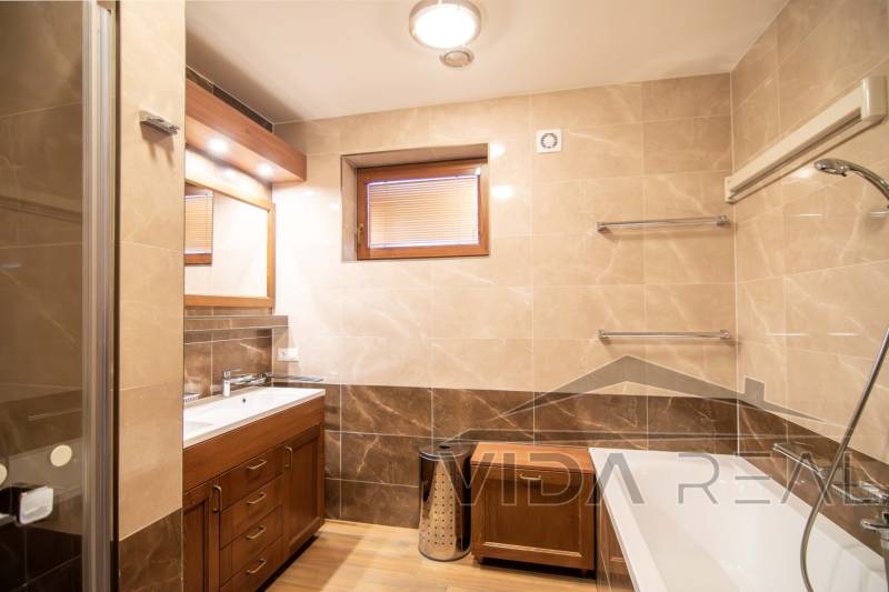 A bathroom in a family house with a bathtub, sink, shower corner, and a floor with a wooden decor.