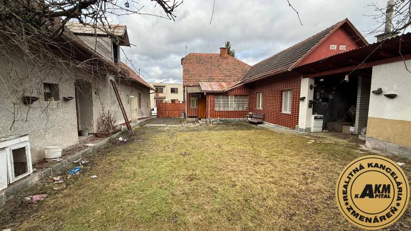 The courtyard of a family house in Babiná with two buildings and a grassy area.