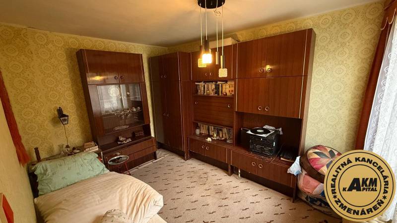 A room in a family house with furniture, a bed, and patterned wallpaper on the walls.