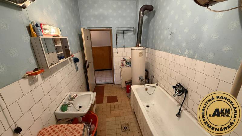 The bathroom in the family house contains a bathtub, a sink, old furniture, and a boiler.