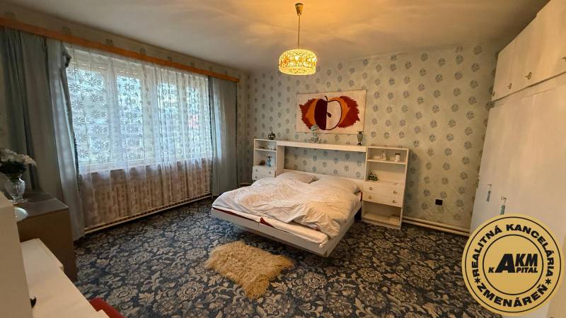 A bedroom in a family house with a floral carpet and a large window.