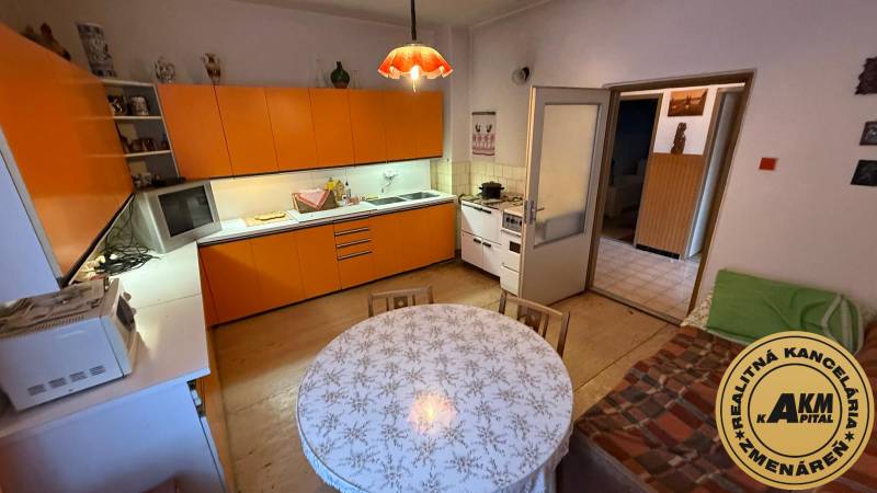 A kitchen in a family house with an orange kitchen unit, table, and a wooden decor floor.