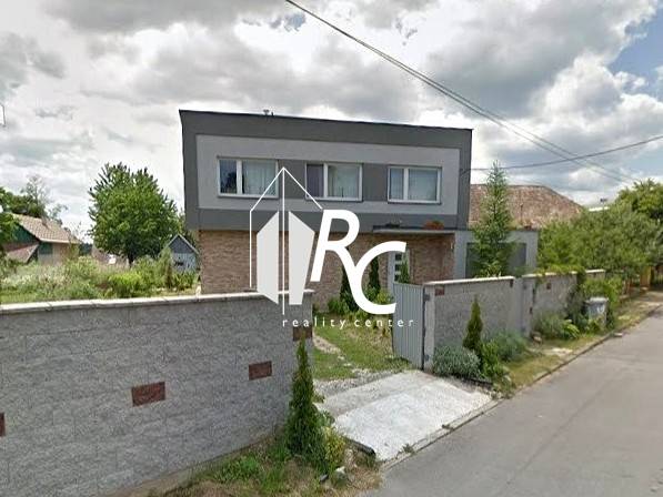 A family house in Bystrička with a landscaped garden and a high fence along the street.