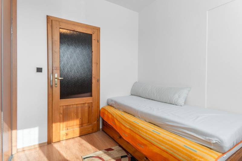 A simple room in a 4-room apartment with a bed and a wooden decor floor.