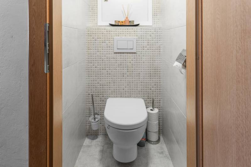 A toilet in a 4-room apartment with tiled walls and storage space.