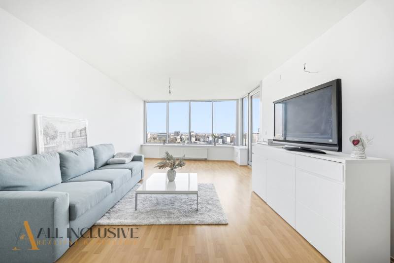 Living room in a two-room apartment with a sofa, television, and wooden decor flooring.