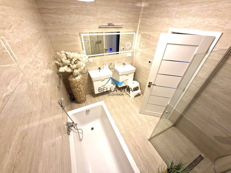 Bathroom in a family house with a bathtub, sink, floral arrangement, and large mirror.