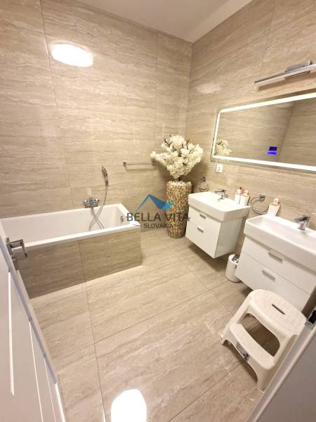 A bathroom in a family house with a bathtub, double sink, and decorative vase.