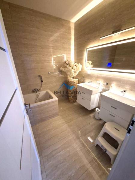 A bathroom in a family house with a bathtub, mirror, and cabinets. Floor with wood decor.