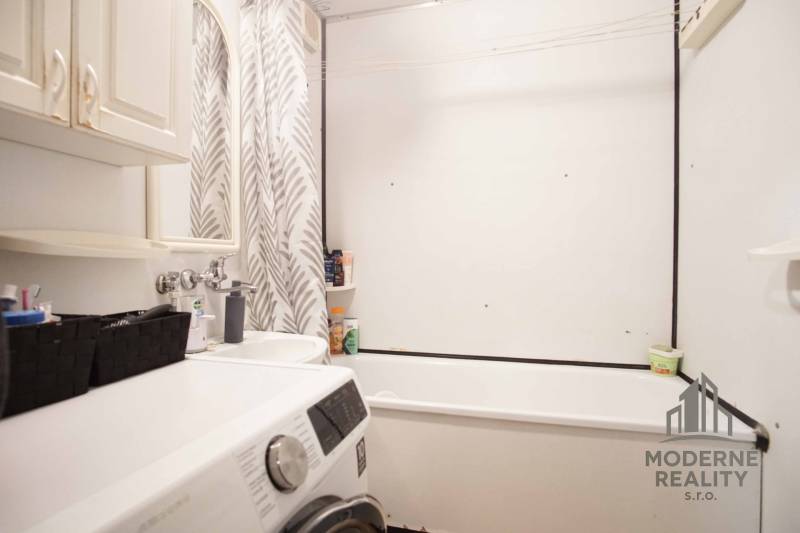 A bathroom in a 3-room apartment with a shower curtain, a washing machine, and storage space.