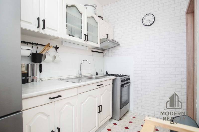 A kitchen in a 3-room apartment with white furniture and a wall clock.