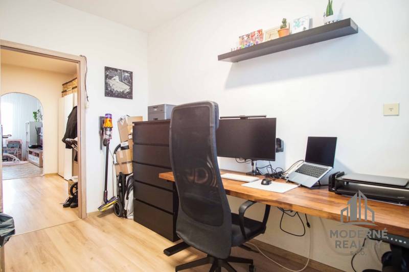 A workspace in a 3-room apartment with a wooden decor floor and a shelf above the desk.