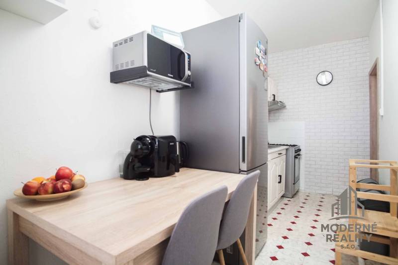 A kitchen in a 3-room apartment with a refrigerator, microwave, and kitchen table.