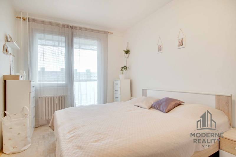 Bedroom in a 3-room apartment with a light-colored bed and dresser, decorated with a plant.